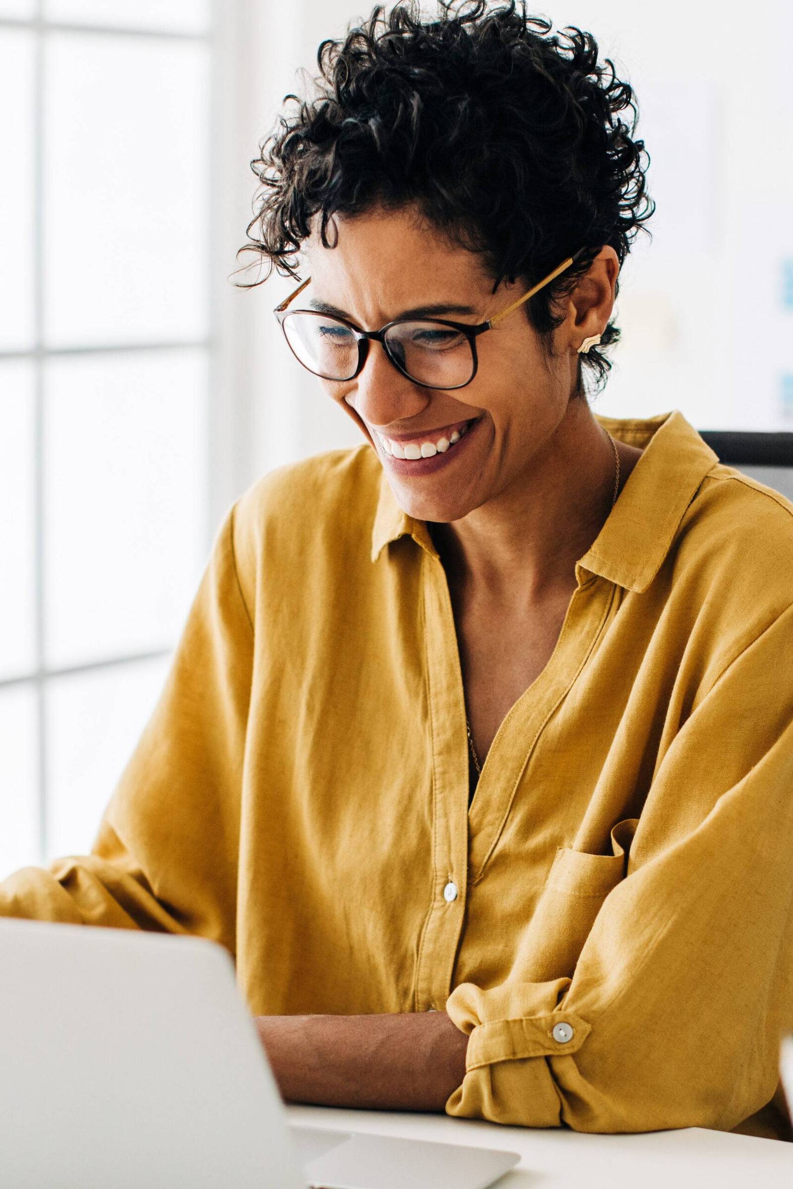 Smiling woman wearing glasses, working on laptop.